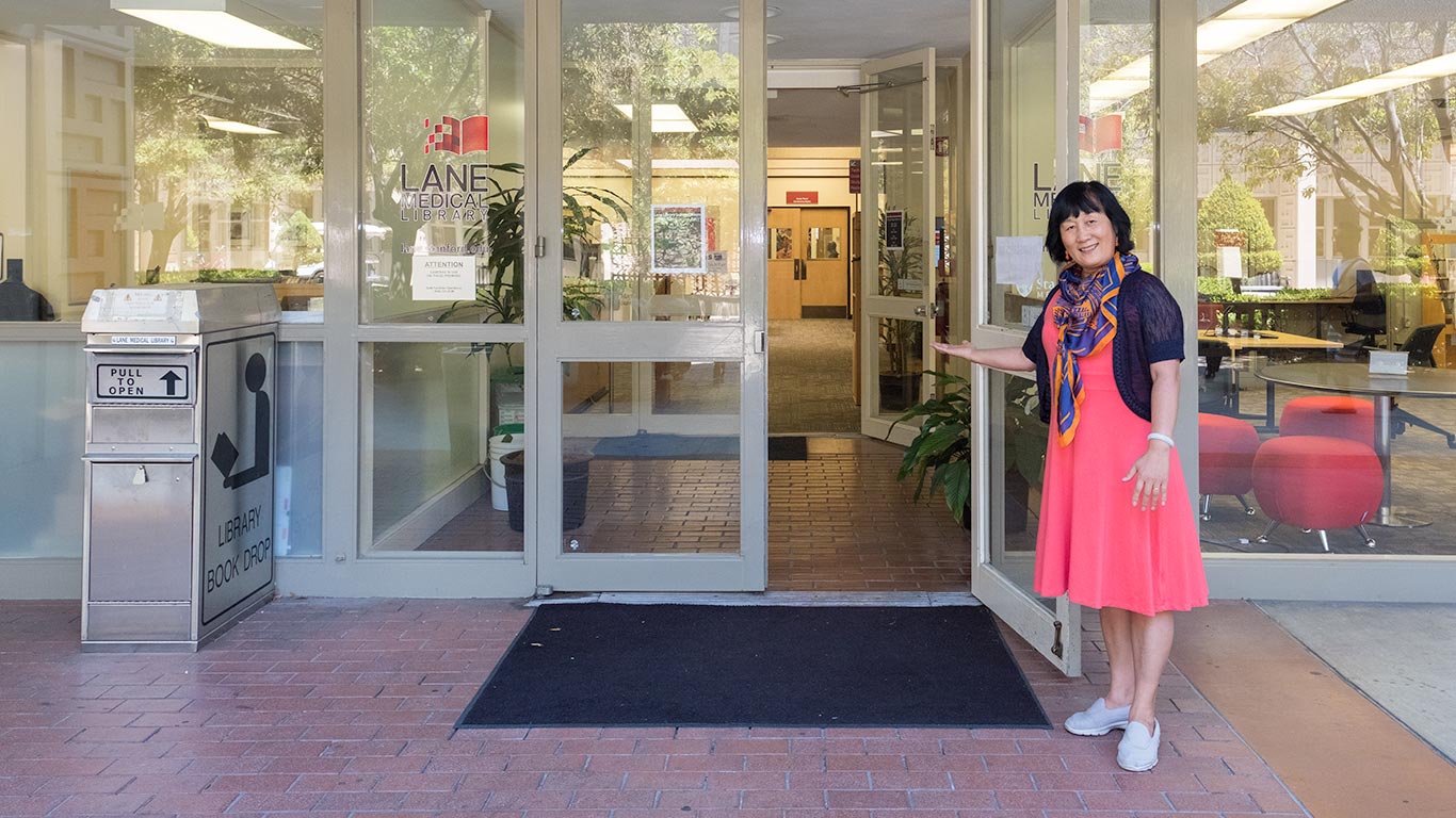 Entrance to the library and library staff member inviting inside throught the doors