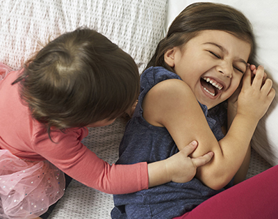 Two toddler kids playing together on a bed