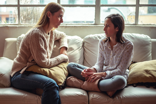 Mother and teen daughter sitting on a couch having a serious discussion