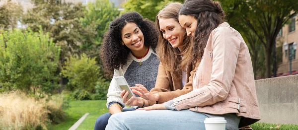 3 women sitting outside using a mobile phone